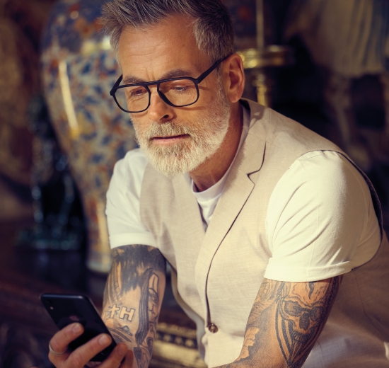 Mann mit Brille blickt auf s Smartphone.