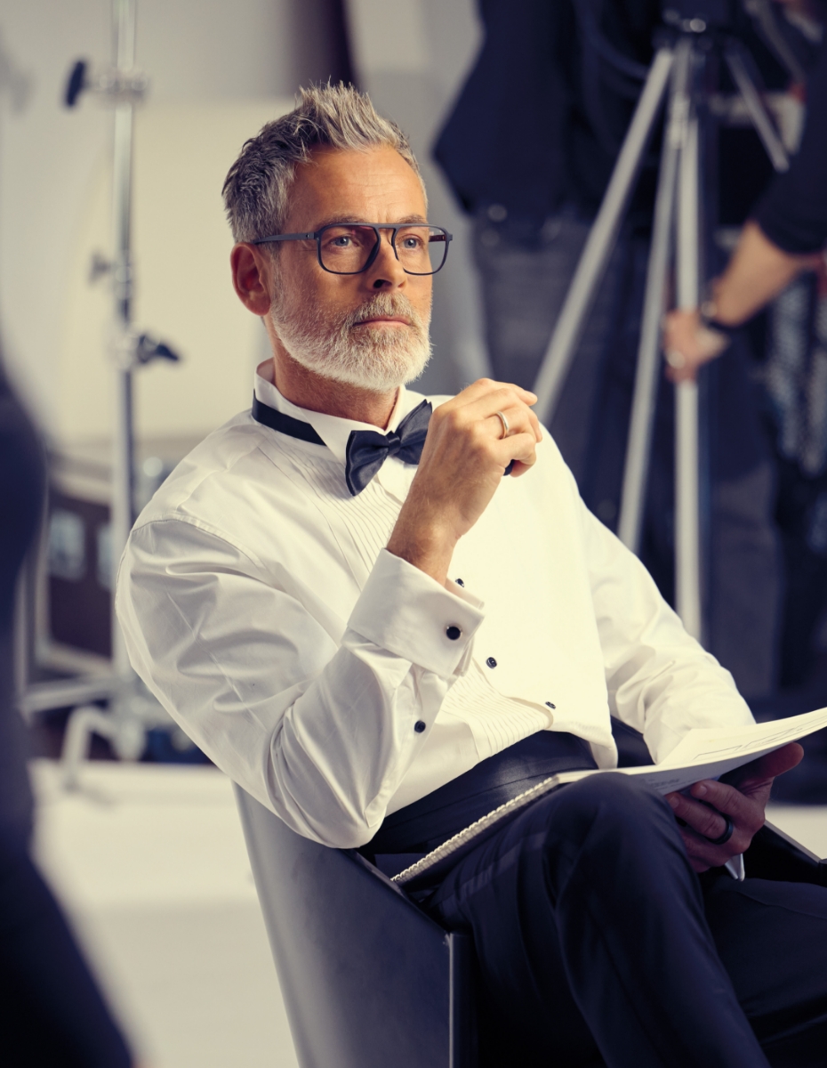 Mann mit grauen Haaren, Anzug und Fliege trägt Brille.