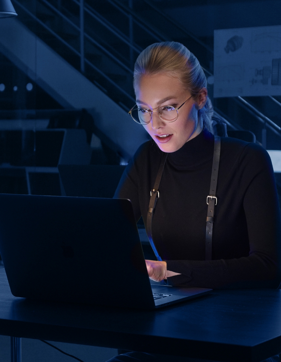 Frau mit Brille arbeitet im Dunklen am Computer.